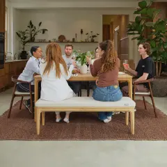 Friends enjoy drinks around a wooden table, showcasing a stylish mix and match of dining chairs and a bench for a relaxed gathering.