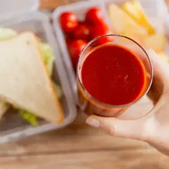 Szklanka z sokiem pomidorowym, obok kanapki i pomidorki koktajlowe. Idealny zestaw na drugie śniadanie.