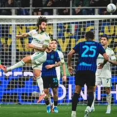 Piłkarz w białej koszulce Inter Mediolan wyskakuje do strzału głową, podczas gdy zawodnik AS Roma z numerem 25 próbuje go zatrzymać.