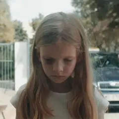 Smutna dziewczynka z sińcami pod oczami, w tle samochód i mężczyzna. Scena z filmu budząca konfuzję.