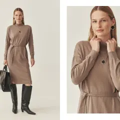 Elegancka, beżowa sukienka boho z paskiem, idealna na jesienne stylizacje. Modelka prezentuje ją z wysokimi kozakami i czarną torebką.