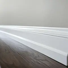 Biały, ozdobny cokół tworzy elegancką linię między ciemną, drewnianą podłogą a jasną ścianą.