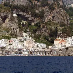Atrani beach club nestled below dramatic cliffs, with colorful buildings cascading down to the sea.