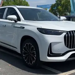 Biały SUV Jaecoo 9 z chromowanym grillem i czarnymi felgami stoi na parkingu.