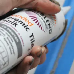 Hand holding a tube of "Sanded Ceramic Caulk" in "19 Pewter" color.