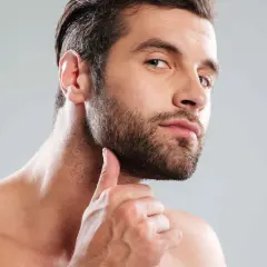 Un homme au regard intense, sa main effleurant sa barbe bien taillée. Une coupe barbe homme parfaite pour un style affirmé.