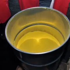 Żółty proszek, być może uran, w metalowym pojemniku. Wokół widać fragmenty czerwonych fartuchów.