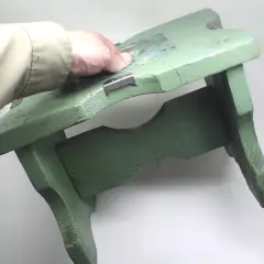Mano che tiene uno sgabello di legno verde, pronto per verniciare con bomboletta spray.