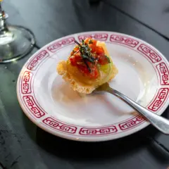 Wykwintny amuse bouche z awokado i pomidorkami na chrupiącym spodzie, podany na talerzyku z czerwonym wzorem.