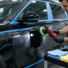 Un homme polit une voiture noire avec une polisseuse. Le travail est soigné, comme un ordre de réparation pour un véhicule de luxe.