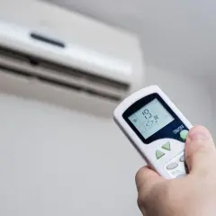 Mando a distancia ajustando la temperatura ideal aire acondicionado para ahorrar energía. Se ve el aire acondicionado y la mano con el control.