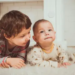 Dwóch braci leży na dywanie. Starszy patrzy na młodszego. Może to przyszli beneficjenci Kinderzuschlag?