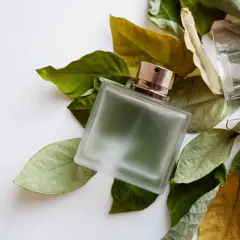 Szklana butelka perfum z metalową nakrętką, otoczona suchymi i zielonymi liśćmi. Zapach fougere, jak spacer po lesie.