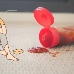 Verzweifelte Person mit Putzmitteln und Schwamm sitzt neben Ketchupfleck auf dem Boden. Der Kampf um den outdoor teppich reinigen beginnt.