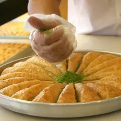 Ręka w rękawiczce posypuje baklavę zielonymi pistacjami. To pyszne ciasto, które warto poznać!