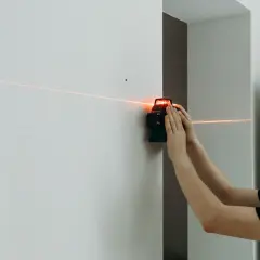 Un homme utilise un niveau laser pour tracer une ligne parfaitement droite sur un mur blanc.