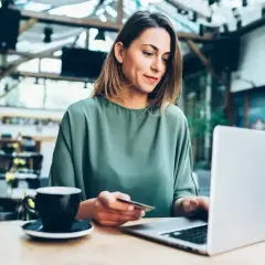 Kobieta z kartą płatniczą w ręku pracuje na laptopie w kawiarni, planując swoje sesje wychodzące.