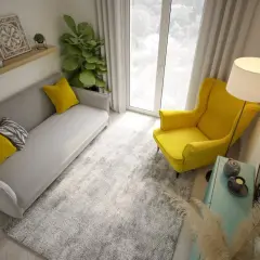 Przytulny, bardzo mały salon w bloku. Szara kanapa z żółtymi poduszkami, żółty fotel, dywan i lampa.