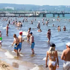 Tłum ludzi cieszy się słońcem i kąpielą w Bałtyku. Woda jest płytka, co idealnie oddaje średnią głębokość Bałtyku.