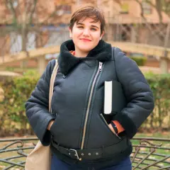 Uśmiechnięta osoba w czarnej, ocieplanej kurtce przejściowej duże rozmiary, trzymająca książkę.
