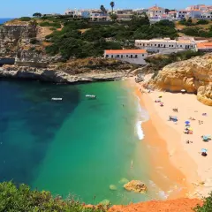 Playa dorada con aguas turquesas y acantilados, ideal para tu plan de algarve en 6 dias. Casas blancas coronan la colina.