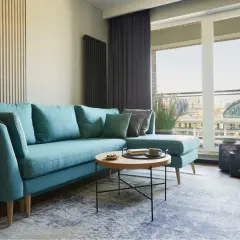 Turkusowa sofa z poduszkami i kocem, niski stolik kawowy z filiżanką kawy. Idealna wysokość ławy do salonu.