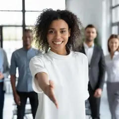Une femme souriante tend la main, prête à aider pour une demande de local gratuit pour association. Son équipe est derrière elle.