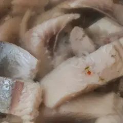 Kawałki kiszonych śledzi w zalewie, niektóre z drobinkami przypraw.
