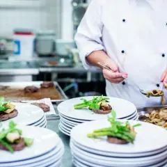 Ein Koch garniert Steaks mit Spargel und Pilzen. Das Gehalt eines Kochs hängt von Erfahrung und Restaurant ab.