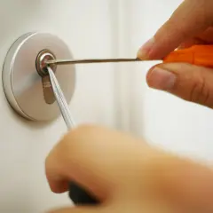 Dłoń używa wytrychu i napinacza do otwarcia zamka w drzwiach.