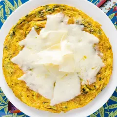 Frittata di bietole dorata e filante, servita su un piatto bianco con un sottobicchiere blu decorato con pesci e foglie.