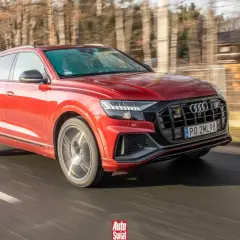 Czerwone Audi SQ8 pędzi po drodze, otoczone rozmazanym lasem.