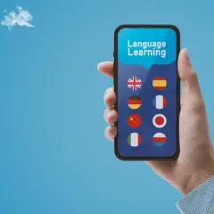 Dłoń trzyma smartfon z aplikacją do nauki języków. Widoczne flagi: Wielkiej Brytanii, Hiszpanii, Niemiec, Francji, Chin, Japonii, Włoch i Polski. Bussu ułatwia podróże.