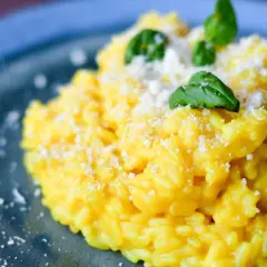 Pyszny, kremowy ryż do risotto, posypany parmezanem i udekorowany listkami bazylii, na niebieskim talerzu.