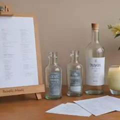 Tablica z listą "WEDDING", butelki, świeca i bukiet kwiatów.
