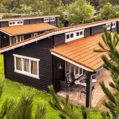 Czarny bungalow z pomarańczowym dachem, otoczony zielenią. To idealne miejsce na wypoczynek.