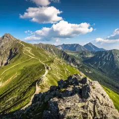 Malownicza ścieżka prowadzi na wejście na Kasprowy. Zielone zbocza Tatr pod błękitnym niebem z chmurami.