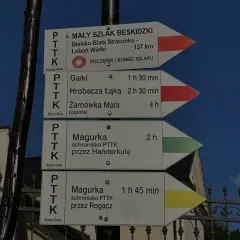 Znaki szlaku turystycznego, w tym czerwony szlak, wskazują drogę do Magurki, Gaików i innych beskidzkich celów.