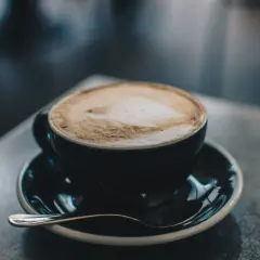 En kopp cappuccino med lattekonst, en av många italienska kaffesorter, står på ett fat med en sked.