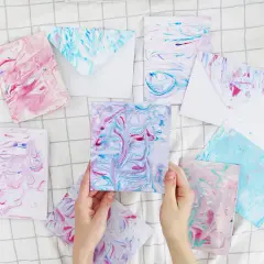 Bunte Karten und Umschläge mit Marmorierungsmuster, die an fließendes Wasser erinnern. Papier marmorieren ist eine kreative Technik.