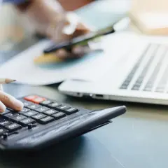 Osoba liczy na kalkulatorze, obok leży laptop. Dowiadujemy się, ile prądu zużywa komputer stacjonarny.