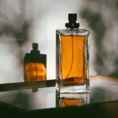 Elegancka butelka perfum z bursztynowym płynem i jej odbicie. Dowiedz się, jak przelać perfumy do innej butelki, by cieszyć się ulubionym zapachem.