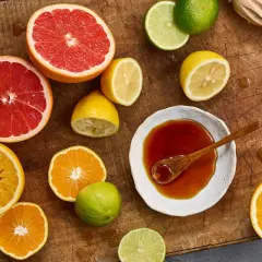 Färska citrusfrukter som apelsiner, grapefrukt och citroner, samt en skål med mörk vätska, antyder ingredienser för ett ponzu recept.
