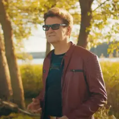 Mężczyzna w skórzanej kurtce, niczym król imperium disco polo, pozuje na tle jesiennego krajobrazu nad jeziorem.