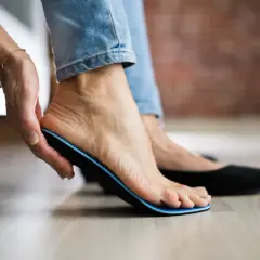 Frau zieht Einlage aus dem Schuh, um Schmerzen nach dem Tragen von Einlagen zu lindern.