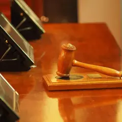 Richterhammer auf einem Holztisch, bereit für das d'hondt verfahren. Drei Bildschirme im Hintergrund.
