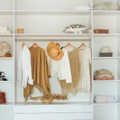 En vit garderob med kläder och accessoarer. En vit skjorta, en brun poncho, en vit kavaj med hatt, en beige virkad topp och en vit klänning hänger på galgar. Hm, bubs, så fint!
