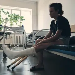 Kobieta z nogą w gipsie i kulami czeka na rehabilitację po złamaniu nogi.