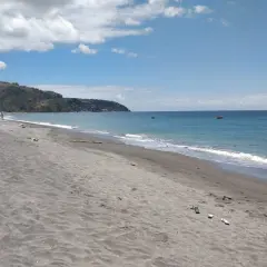 Plaża na wyspie Dominika z ciemnym piaskiem, turkusową wodą i zielonymi wzgórzami w tle.