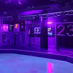 Der leere Dancefloor im Club 23 Rothenburg, beleuchtet in lila und blauem Licht. Hohe Tische und Barhocker stehen bereit.